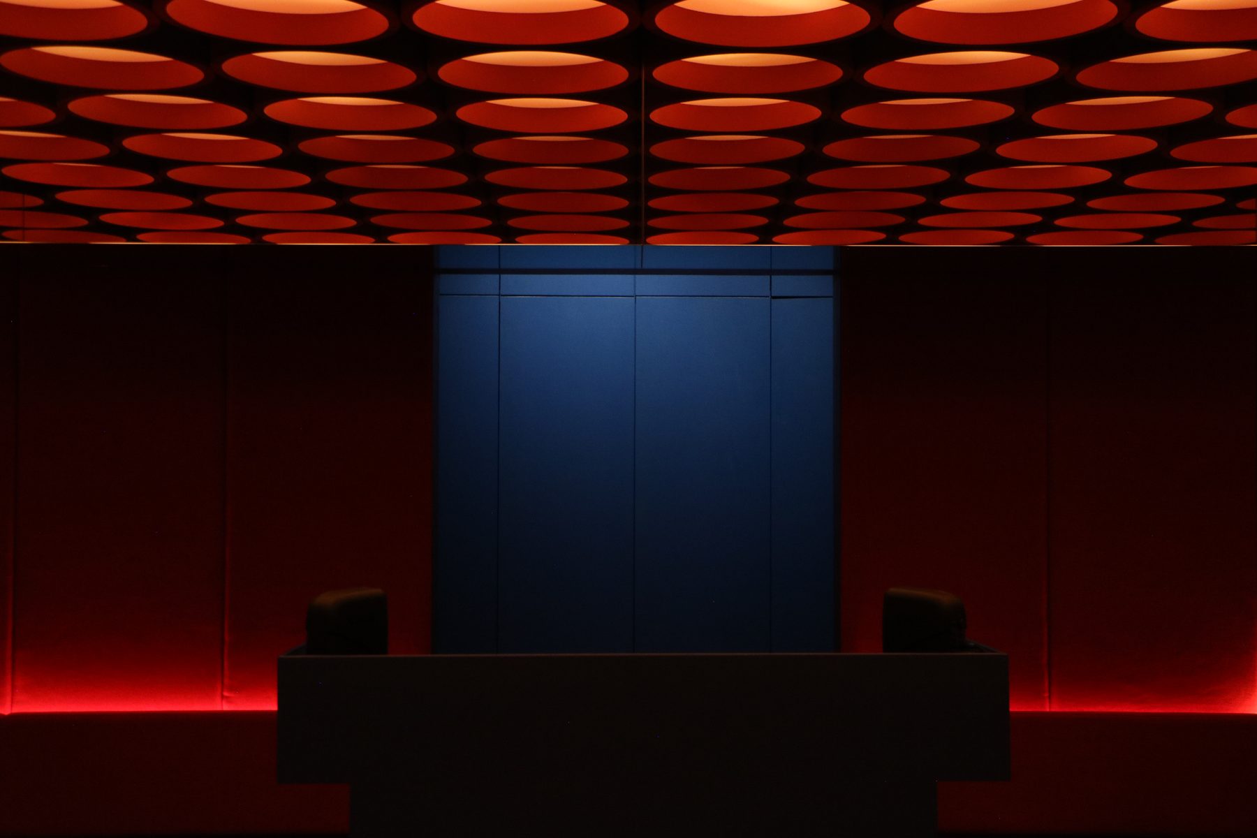 Interior de ROSSO: sillones rojos, luz azul al fondo y techo de círculos